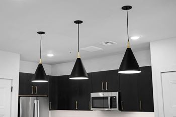A kitchen with black cabinets and a stainless steel refrigerator and black pendant lights hanging from the
